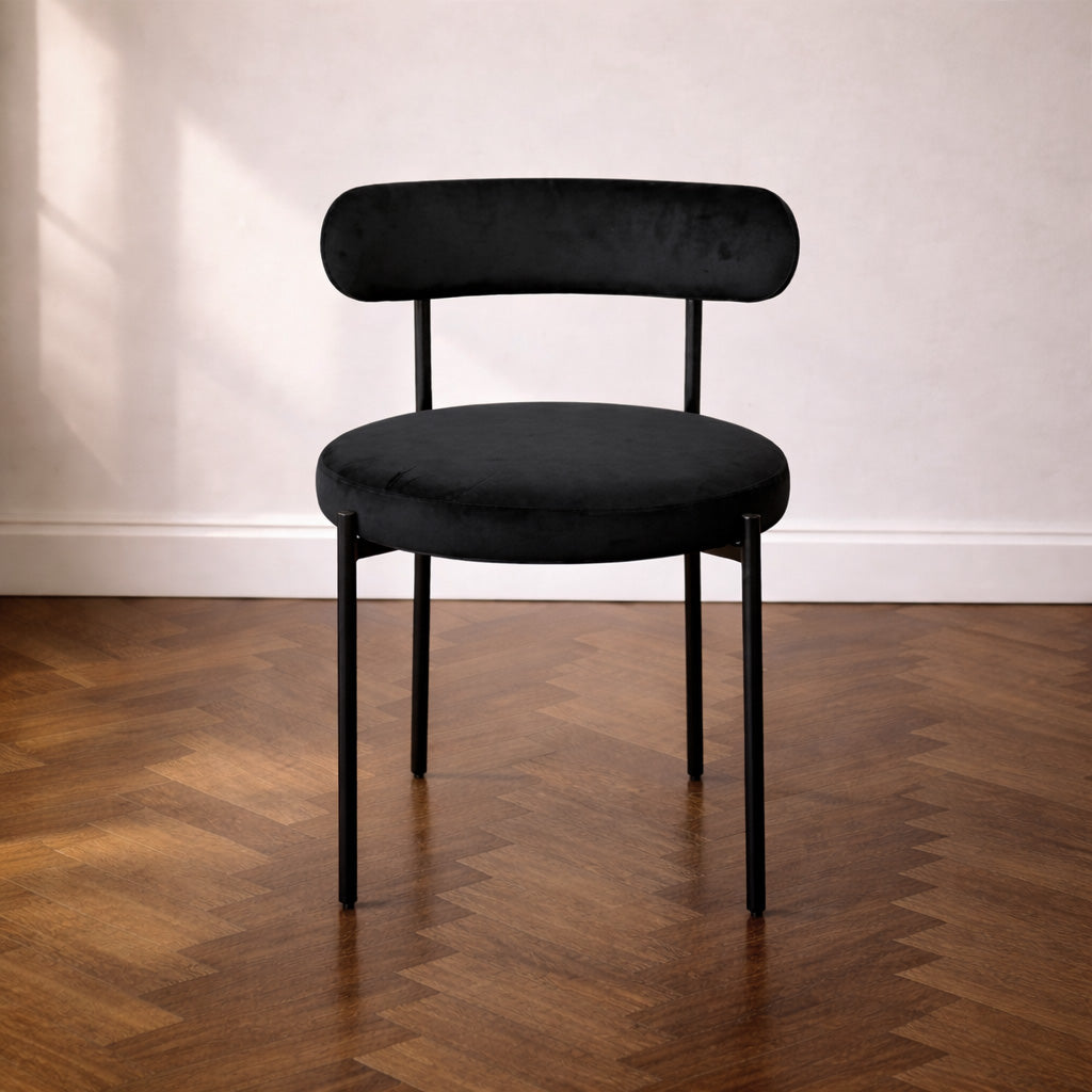 Contemporary black velvet chair on a wooden floor with a white wall background