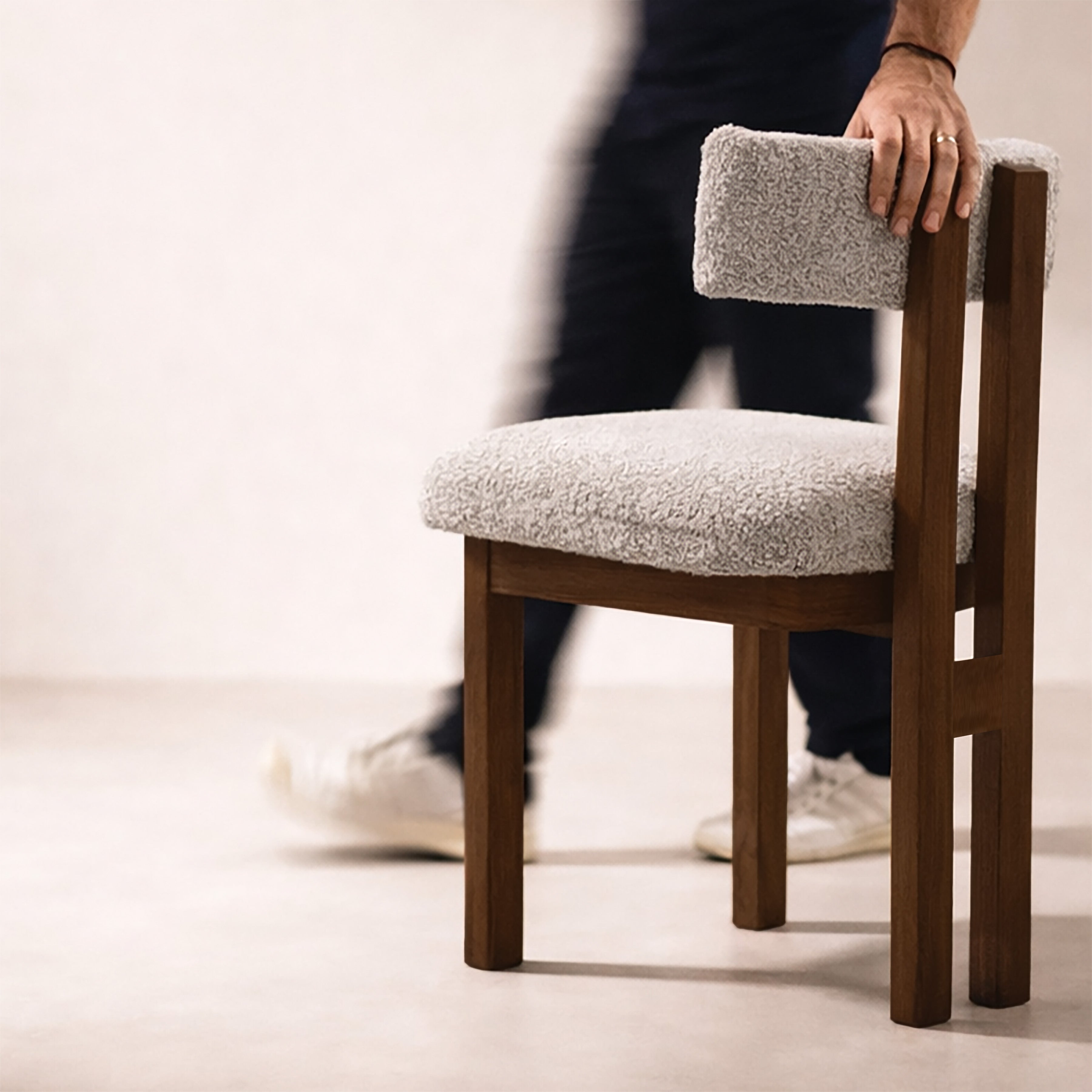 Person holding a wooden chair with a gray textured boucle cushioned seat and backrest.