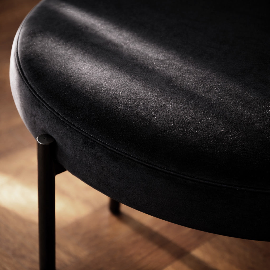 Close-up product shot of a black velvet cushioned stool on a wooden floor