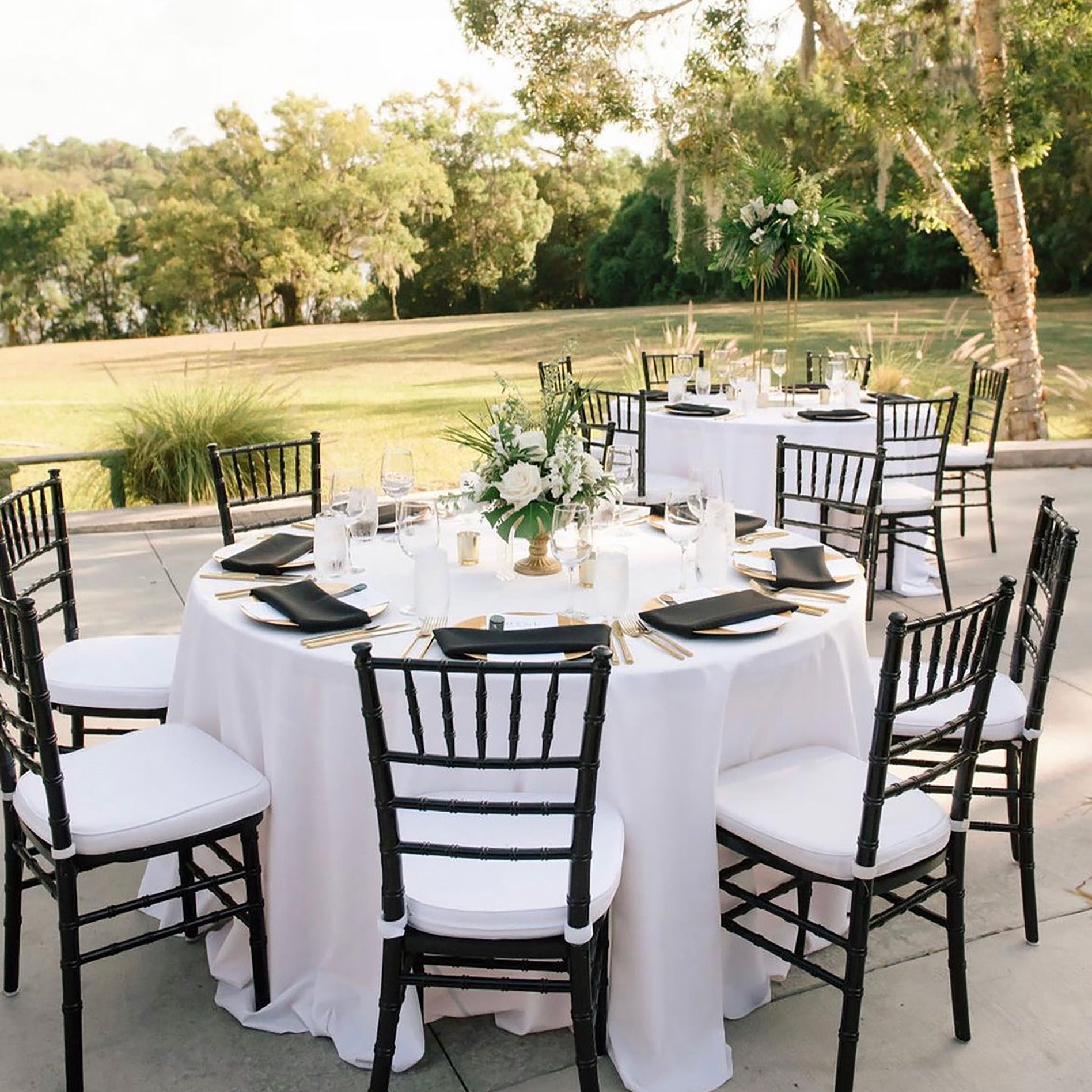 Outdoor wedding setup with tables, chairs, and floral arrangements in a backyard.